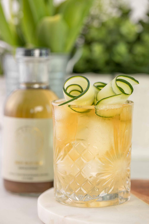 Closeup of Green Earth Sour cocktail with bottle of Kvas Ginger Wildflower Simple Syrup