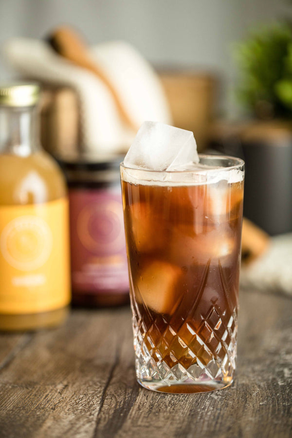 Closeup of Ko-Ko Kola cocktail next to Kvas Whisky Sour Syrup bottle