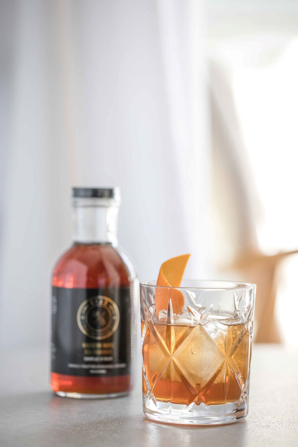 Closeup of The King in the North Old Fashioned cocktail next to bottle of Kvas Northern Maple Old Fashioned Simple Syrup