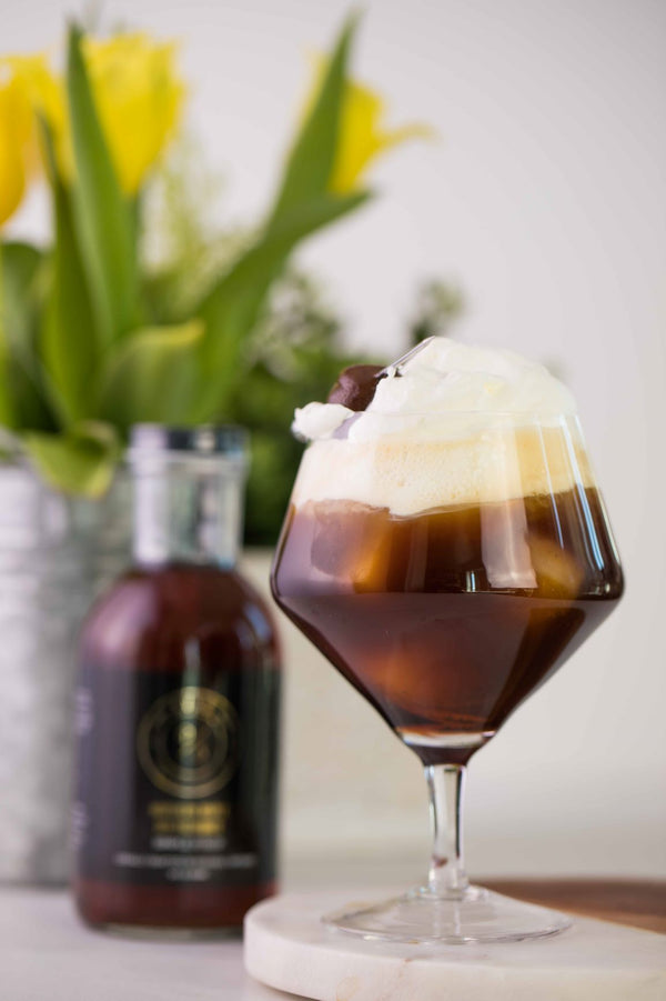 Closeup of Kvas Siggy Coffee cocktail next to bottle of Kvas Northern Maple Old Fashioned Simple Syrup