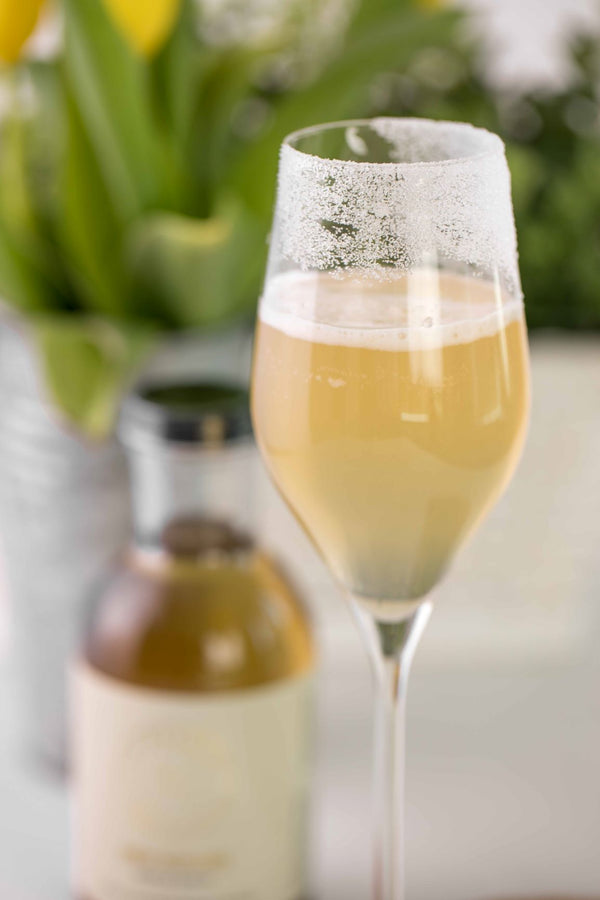 Closeup of Kvas Peach Crusta cocktail next to bottle of Kvas Ginger Wildflower Simple Syrup